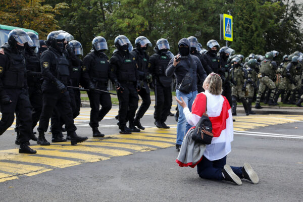 Một người biểu tình với lá cờ trắng-đỏ-trắng lịch sử của Belarus quỳ gối trước các nhân viên thực thi pháp luật trong một cuộc biểu tình chống lại sự tàn bạo của cảnh sát ở Minsk vào ngày 13/9/2020. (Ảnh Tut.By / Reuters)