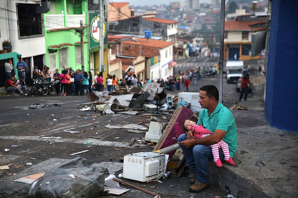 Một bức ảnh tệp tin từ ngày 8/3/2014, cho thấy một người cha và con gái đang nghỉ ngơi trong khi ai đó giữ chỗ của họ từ trước khi mặt trời mọc, trong một hàng dài chờ mua thực phẩm tại một siêu thị ở San Cristobal, Venezuela. (Ảnh John Moore / Getty)