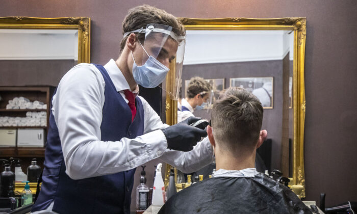 Một thợ cắt tóc đeo khẩu trang và tấm bảo vệ cho một khách hàng tại một tiệm cắt tóc ở Prague, Cộng hòa Séc, vào ngày 11/5/2020. (Ảnh Gabriel Kuchta / Getty Images)