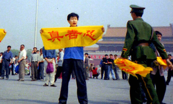 Một công an Trung Quốc tiếp cận một học viên Pháp Luân Công tại Quảng trường Thiên An Môn ở Bắc Kinh khi vị này cầm một tấm biểu ngữ có các Hán tự “Chân-Thiện-Nhẫn”, là những nguyên lý cốt lõi của Pháp Luân Công. (Ảnh được đăng dưới sự cho phép của Minghui.org)