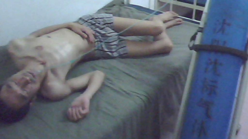 Đoạn phim quay bí mật từ Trại Lao động Cưỡng bức Mã Tam Gia cho thấy một học viên Pháp Luân Công nằm trên giường sau khi bị tra tấn vì phản đối cuộc bức hại. Đoạn phim này được quay trong thời gian diễn ra Thế vận hội Bắc Kinh năm 2008. (Ảnh: Đăng dưới sự cho phép của Yu Ming)