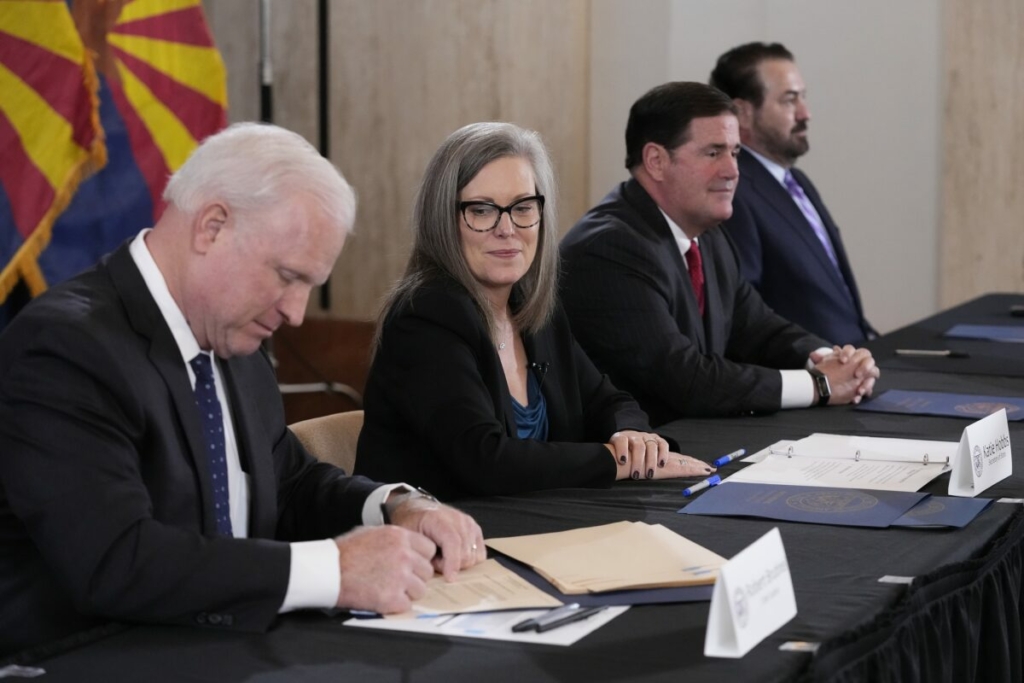 Chánh án Tòa án Tối cao Arizona Robert Brutinel (bên trái) ký vào tài liệu kiểm đếm chính thức cuộc tổng tuyển cử ở Arizona khi bà Katie Hobbs, thống đốc đắc cử thuộc Đảng Dân Chủ và Tổng thư ký tiểu bang đương nhiệm (thứ hai từ trái sang) quan sát, trong khi Thống đốc Đảng Cộng Hòa Arizona Doug Ducey (thứ hai từ phải sang), và Tổng Chưởng lý Arizona Mark Brnovich (bên phải) cùng ngồi vào bàn trong buổi lễ ký xác nhận tại Tòa nhà Cơ quan Lập pháp Arizona ở Phoenix, Arizona, hôm 05/12/2022. (Ảnh: Ross D. Franklin/Pool/AP Photo)