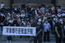 Người dân giương biểu ngữ và hô vang khẩu hiệu trong một cuộc biểu tình ở lối vào một chi nhánh của ngân hàng trung ương Trung Quốc tại thành phố Trịnh Châu, thuộc tỉnh Hà Nam, miền trung Trung Quốc, hôm 10/07/2022. (Ảnh: Yang/AP Photo)