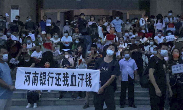 Người dân giương biểu ngữ và hô vang khẩu hiệu trong một cuộc biểu tình ở lối vào một chi nhánh của ngân hàng trung ương Trung Quốc tại thành phố Trịnh Châu, thuộc tỉnh Hà Nam, miền trung Trung Quốc, hôm 10/07/2022. (Ảnh: Yang/AP Photo)