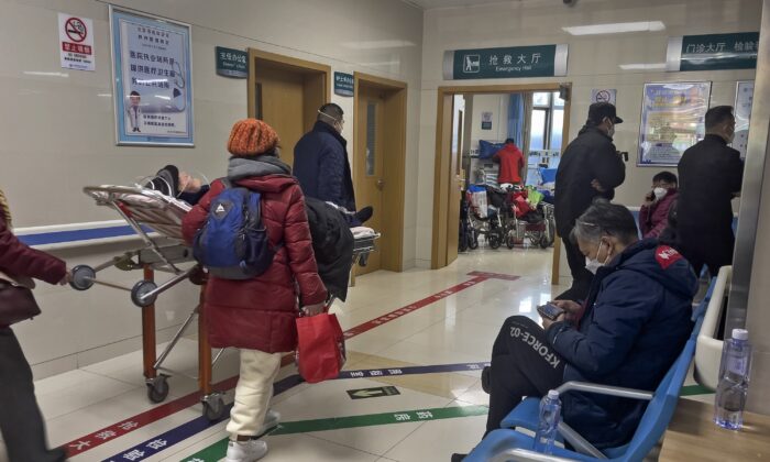 Một người đàn ông (Phải) lướt điện thoại thông minh của mình trên một băng ghế chờ ngoài hành lang, trước mặt là một bệnh nhân lớn tuổi đang được đưa vào phòng cấp cứu tại một bệnh viện ở Bắc Kinh hôm 07/01/2023. (Ảnh: Andy Wong/AP Photo)