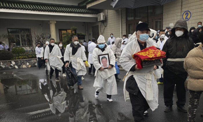 Một người đưa tang khiêng di hài hỏa táng của người thân trong khi ông và những người khác mặc trang phục tang lễ màu trắng truyền thống, trong một đám tang ở Thượng Hải. (Ảnh: Kevin Frayer/Hình ảnh Getty)