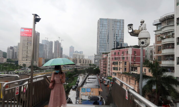 Một người phụ nữ cầm chiếc dù đi trên một cây cầu dành cho khách bộ hành có camera giám sát, gần Thảo Bộ ở huyện La Hồ, thành phố Thâm Quyến, tỉnh Quảng Đông, Trung Quốc, hôm 05/07/2022. (Ảnh: David Kirton/Reuters)