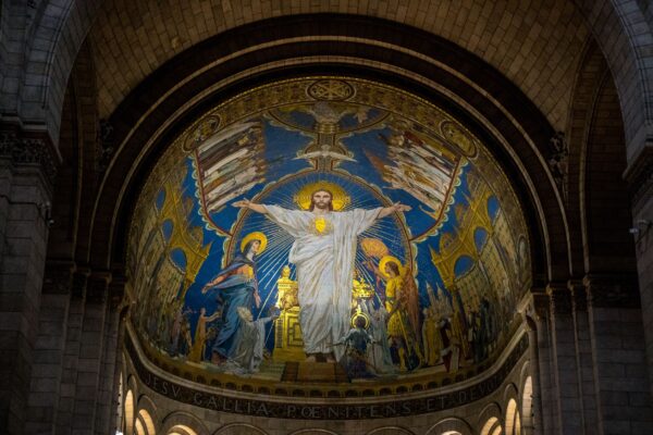 Một trong những điểm nhấn của vương cung thánh đường Sacré-Coeur chính là bức tranh khảm mosaic ở phần hậu cung hình bán nguyệt. Bức tranh này bao gồm 25,000 mảnh gốm tráng men và mạ vàng, và bao phủ khoảng 1,558 feet vuông. Việc lựa chọn màu xanh dương và màu vàng kim là thường thấy trong phong cách Byzantine, cũng như những mái vòm đôi và lối đi có mái vòm. Là một trong những bức tranh khảm mosaic lớn nhất trên thế giới, nhân vật ở giữa tượng trưng cho Chúa Giê-su trong trang phục màu trắng, dang rộng cánh tay dâng hiến trái tim của Ngài. Những nhân vật ở chung quanh Ngài là Đức mẹ Đồng Trinh Mary, Tổng Lãnh Thiên Thần Michael, và Thánh Joan xứ Arc. Ở phần đáy của bức tranh khảm này có dòng chữ bằng tiếng Latin: “Tình yêu tha thiết, sự sám hối, và lòng biết ơn của Pháp quốc dâng hiến đến Thánh Tâm của Chúa Jesus.” (Ảnh: Cynthia Liang/Shutterstock)