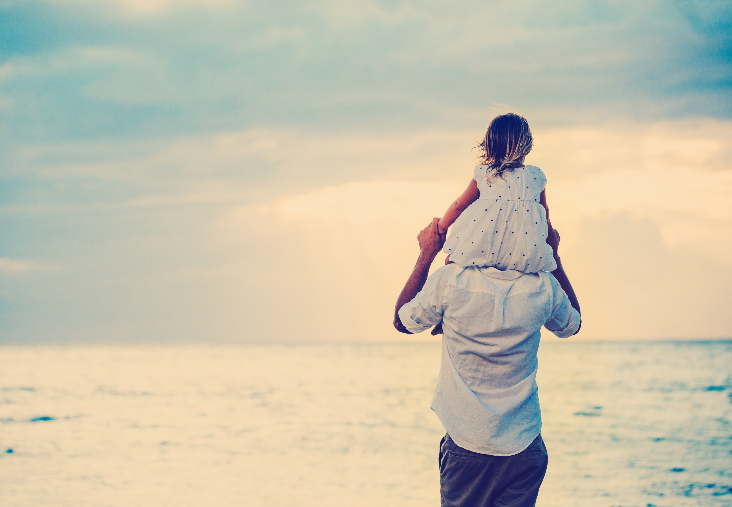 Một cô bé ngồi trên vai cha mình và nhìn ra biển. (Ảnh: Shutterstock)