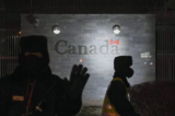 Một lính canh cố gắng ngăn việc chụp ảnh khi anh và một công an khác đang tuần tra bên ngoài Đại sứ quán Canada ở Bắc Kinh vào ngày 14/01/2019. (Ảnh: Greg Baker/AFP qua Getty Images)