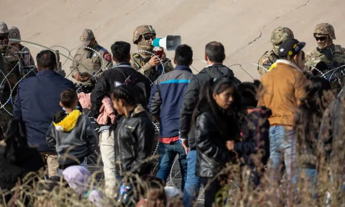 Một binh sĩ thuộc Lực lượng Vệ binh Quốc gia Texas nói chuyện với những người nhập cư tại khu vực có nhiều người vượt biên trái phép dọc theo sông Rio Grande ở thành phố El Paso, Texas, vào ngày 20/12/2022. (Ảnh: John Moore/Getty Images)