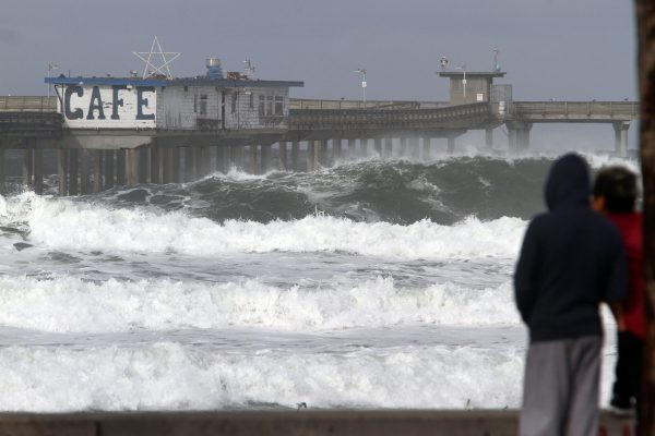 Một số người đang xem những con sóng lớn đập vào bãi biển trên Bến tàu Ocean Beach đã bị đóng cửa do sóng lớn sau những cơn bão mạnh ở San Diego hôm 07/01. (Ảnh: Bill Wechter/AFP/Getty Images)