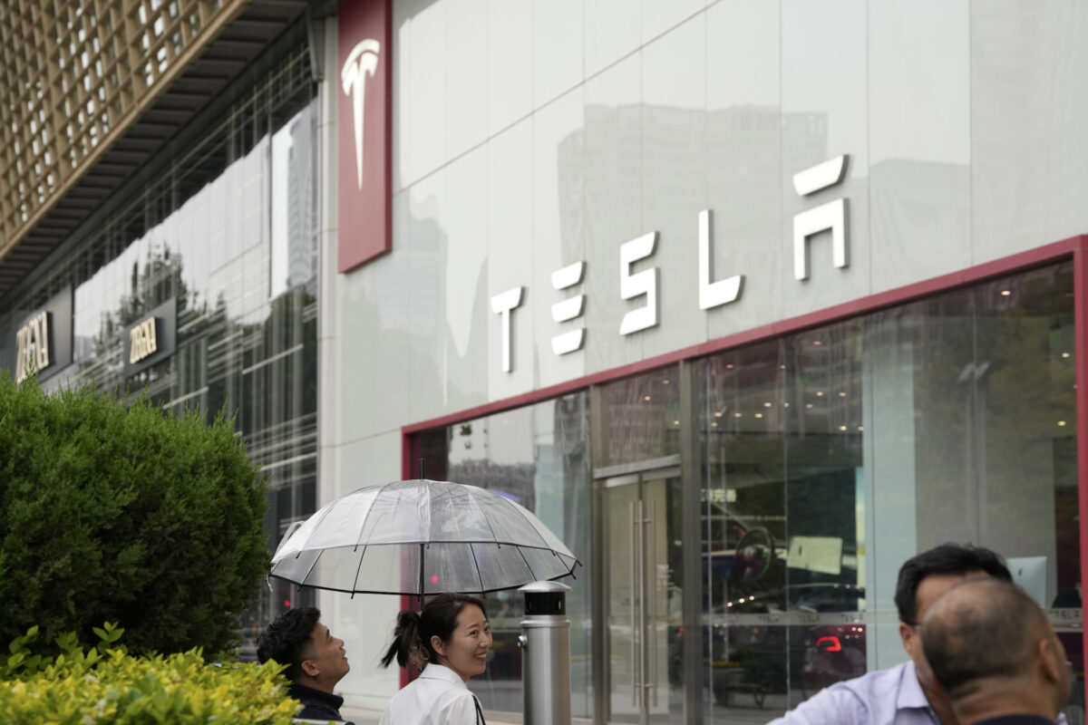 Các nhân viên trò chuyện dưới một cây dù bên ngoài phòng trưng bày Tesla ở Bắc Kinh, Trung Quốc, hôm 30/05/2023. (Ảnh: Ng Han Guan/AP Photo)