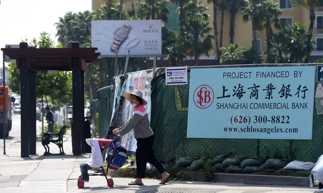 Một người phụ nữ đẩy xe đẩy ngang qua một biểu ngữ tại một dự án xây dựng do Ngân hàng Thương mại Thượng Hải tài trợ ở San Gabriel, California, hôm 17/05/2016. (Ảnh: Frederic J. Brown /AFP/Getty Images)