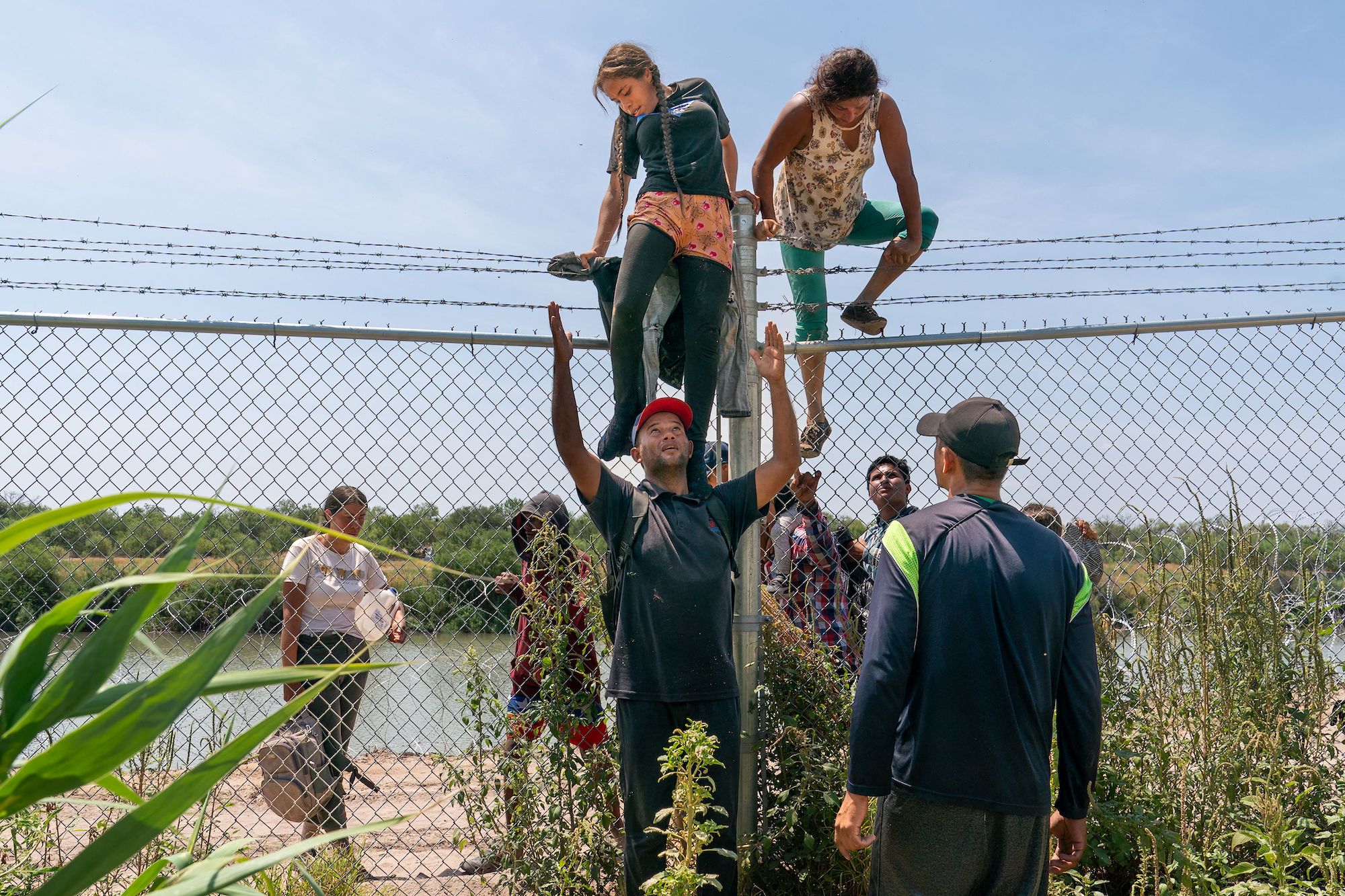 Những người nhập cư bất hợp pháp giúp nhau trèo qua hàng rào thép gai vào Hoa Kỳ từ Mexico, ở Eagle Pass, Texas, hôm 25/08/2023. (Ảnh: Suzanne Cordeiro/AFP qua Getty Images)