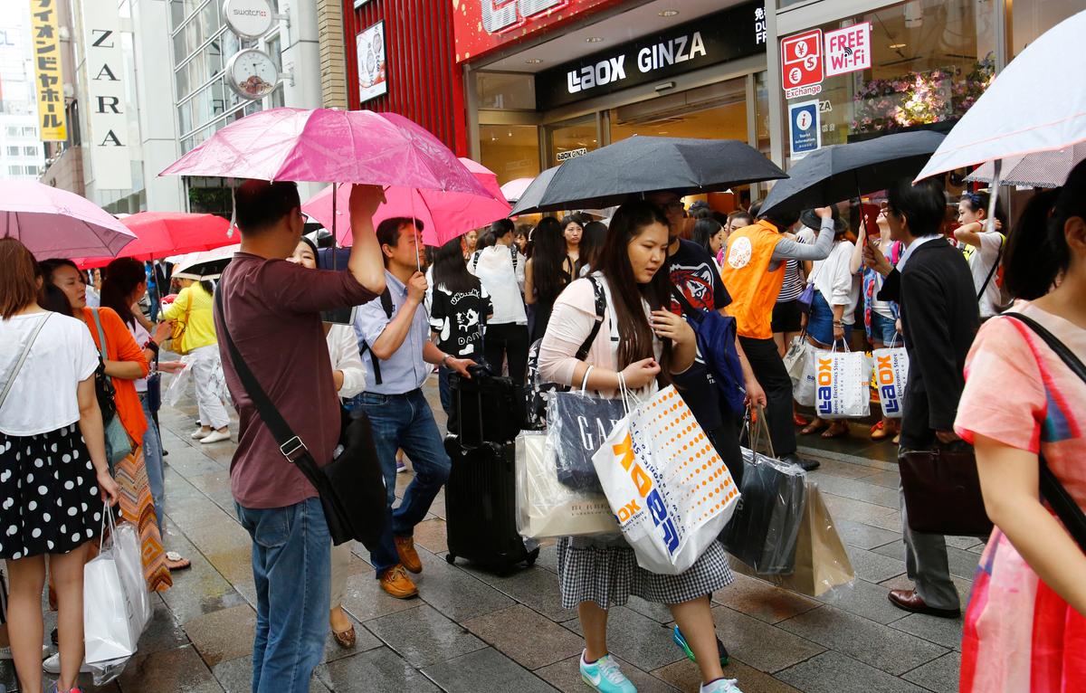 Trong bức ảnh ngày 17/06/2015 này, khách du lịch Trung Quốc cầm túi mua sắm đang chờ xe buýt tham quan trước một cửa hàng điện tử giảm giá ở quận Ginza của Tokyo. (Ảnh: AP Photo/Shizuo Kambayashi)