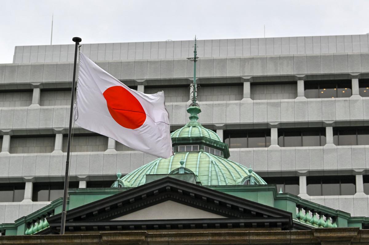 Quốc kỳ Nhật Bản tung bay trên tòa nhà trụ sở chính của Ngân hàng Nhật Bản (BoJ) (phía dưới) ở Tokyo hôm 27/04/2022. (Ảnh: Kazuhiro Nogi/AFP qua Getty Images)
