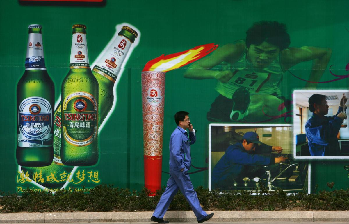 Một công nhân đi ngang qua bảng quảng cáo có hình bia và Ngọn đuốc Olympic tại Nhà máy bia Thanh Đảo, nhà máy bia lớn nhất Trung Quốc và là Nhà tài trợ bia nội địa chính thức cho Thế vận hội Olympic Bắc Kinh 2008 tại Thanh Đảo, tỉnh Sơn Đông, Trung Quốc, vào 25/04/2008. (Ảnh: Trung Quốc/Getty Images)