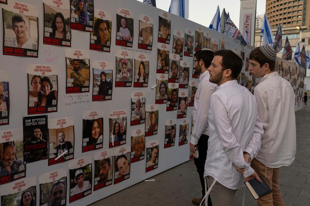 Các thanh niên Israel xem những bức ảnh về những người Israel mất tích và bị giam giữ ở Gaza, được trưng bày trên một bức tường ở Tel Aviv, hôm 20/10/2023. (Ảnh: AP Photo/ Petros Giannakouris)