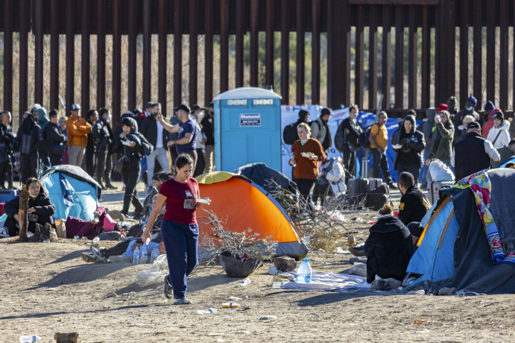 Những người nhập cư bất hợp pháp đã đi qua một khoảng trống trên bức tường biên giới Hoa Kỳ đang chờ các nhân viên Tuần tra Biên giới đến giải quyết thủ tục, ở Jacumba, California, hôm 07/12/2023. (Ảnh: John Fredricks/The Epoch Times)