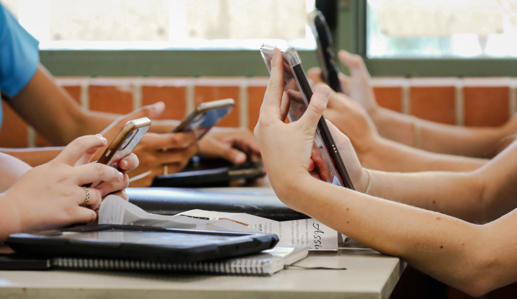 Học sinh trung học ngồi ở bàn cầm nhiều thiết bị kỹ thuật số như điện thoại và máy điện toán bảng (tablet) trong giờ học. (Ảnh: LBeddoe/Shutterstock)