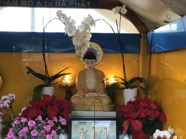 Bức tượng Phật lúc đầu, chung quanh được trang trí bằng những bông hoa, với phần áo choàng được sơn mới màu nâu, hôm 05/12/2023. (Ảnh: Helen Billings/The Epoch Times)