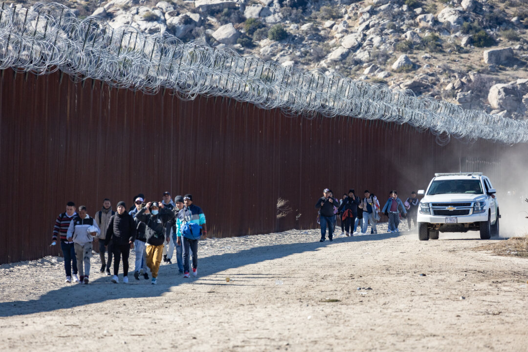Những người nhập cư bất hợp pháp đã đi qua một khoảng trống trên bức tường biên giới Hoa Kỳ, và họ đang chờ các nhân viên Tuần tra Biên giới đến giải quyết, ở Jacumba, California, hôm 07/12/2023. (Ảnh: John Fredricks/The Epoch Times)
