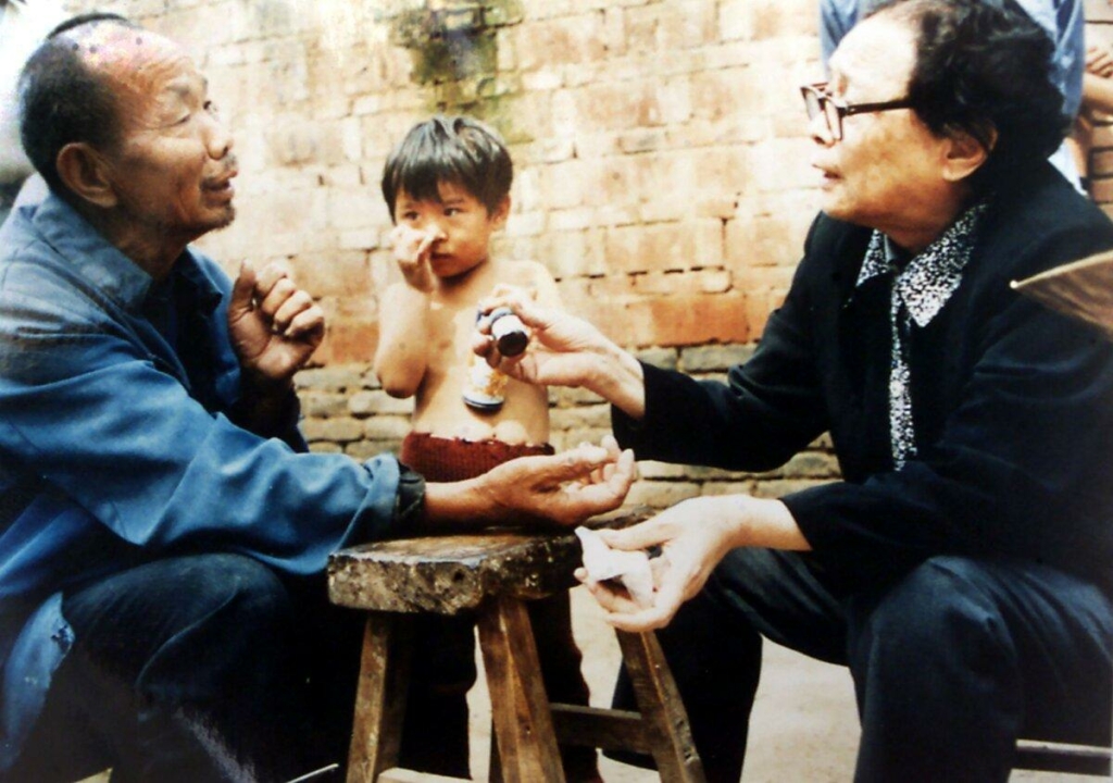 Trong bức ảnh không đề ngày tháng này, bác sĩ đã về hưu Cao Diệu Khiết (Gao Yaojie), 74 tuổi, (bên phải) bôi thuốc lên cánh tay của một dân làng khi bà giúp đỡ những người đến từ những ngôi làng AIDS bị cộng đồng xa lánh ở tỉnh Hà Nam, miền trung Trung Quốc. (Ảnh: STR/AFP qua Getty Images)