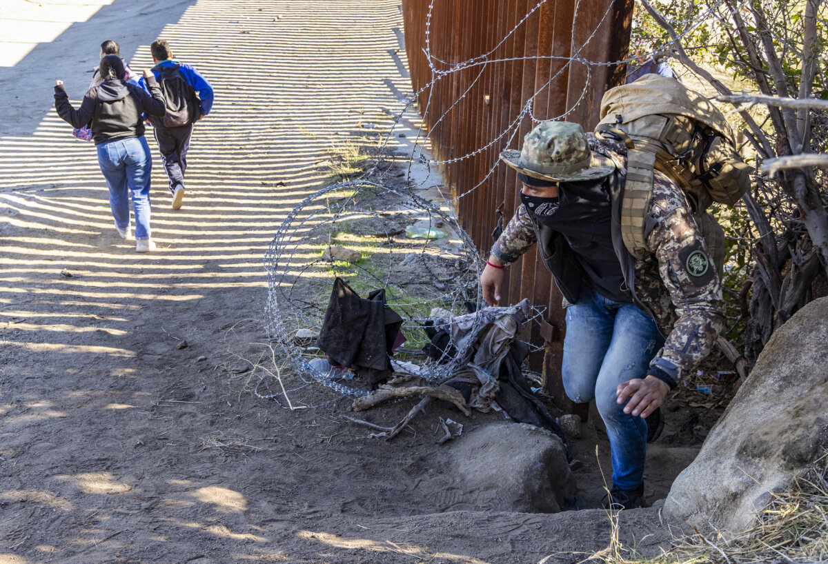 Những người nhập cư bất hợp pháp đi qua một khe hở dọc bức tường biên giới Hoa Kỳ để chờ các nhân viên Biên phòng giải quyết ở Jacumba, California, hôm 07/12/2023. (Ảnh: John Fredricks/The Epoch Times)