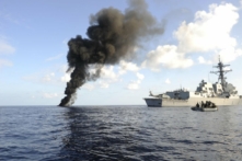 Trong bức ảnh phân phát đi này của Hải quân Hoa Kỳ, khu trục hạm mang phi đạn dẫn đường USS Farragut (DDG 99) lớp Arleigh Burke đi ngang qua làn khói bốc lên từ một tàu nhỏ bị tình nghi là cướp biển mà chiến hạm này đã vô hiệu hóa ở Vịnh Aden vào ngày 31/03/2010. USS Farragut là một phần của Lực lượng Đặc nhiệm Liên hợp 151, một lực lượng đặc nhiệm đa quốc gia được thành lập để tiến hành các hoạt động chống cướp biển ở Vịnh Aden. (Ảnh: Chuyên gia Truyền thông Đại chúng cấp 1 Cassandra Thompson/Hải quân Hoa Kỳ qua Getty Images)