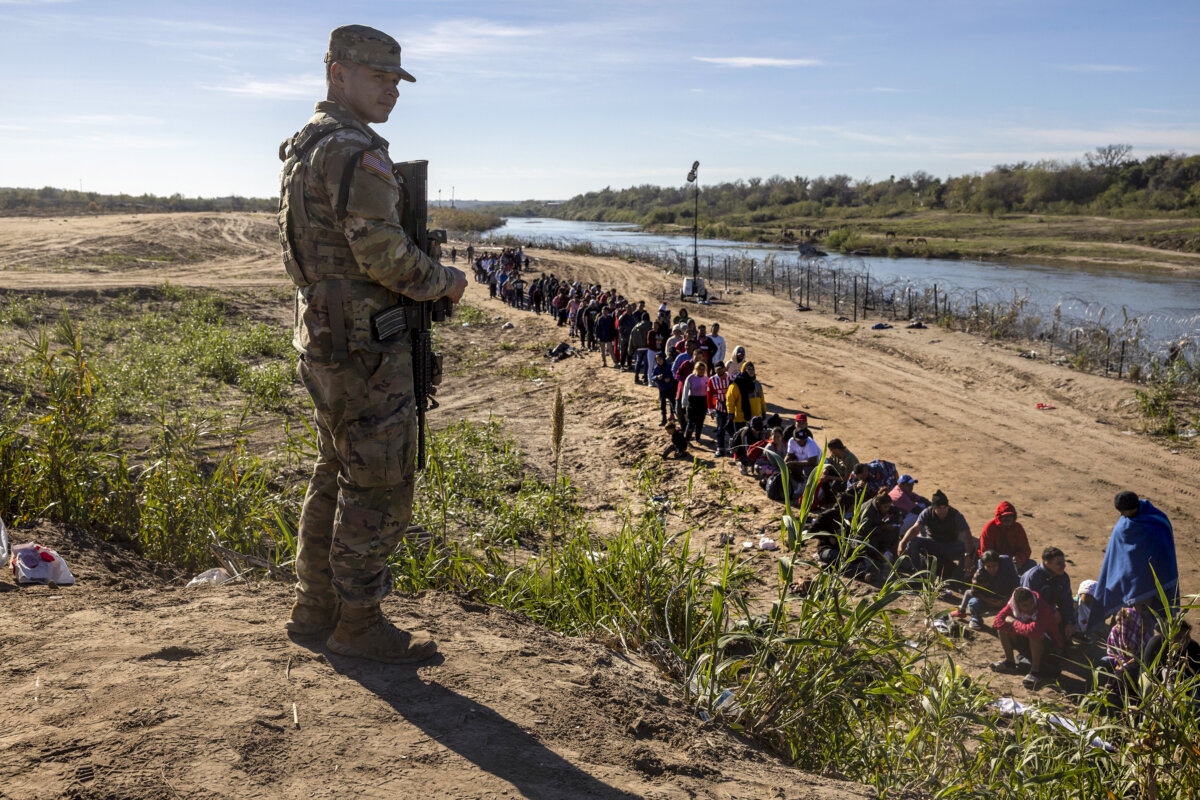 Một người lính Vệ binh Quốc gia Texas trông chừng một nhóm hơn 1,000 người di cư đã vượt sông Rio Grande từ Mexico ở Eagle Pass, Texas, hôm 18/12/2023. (Ảnh: John Moore/Getty Images)