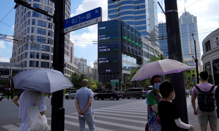 Người đi bộ chờ băng qua đường tại ngã ba gần một màn hình chỉ số chứng khoán lớn ở Thượng Hải, Trung Quốc, hôm 03/08/2022. (Ảnh: Aly Song/Reuters)