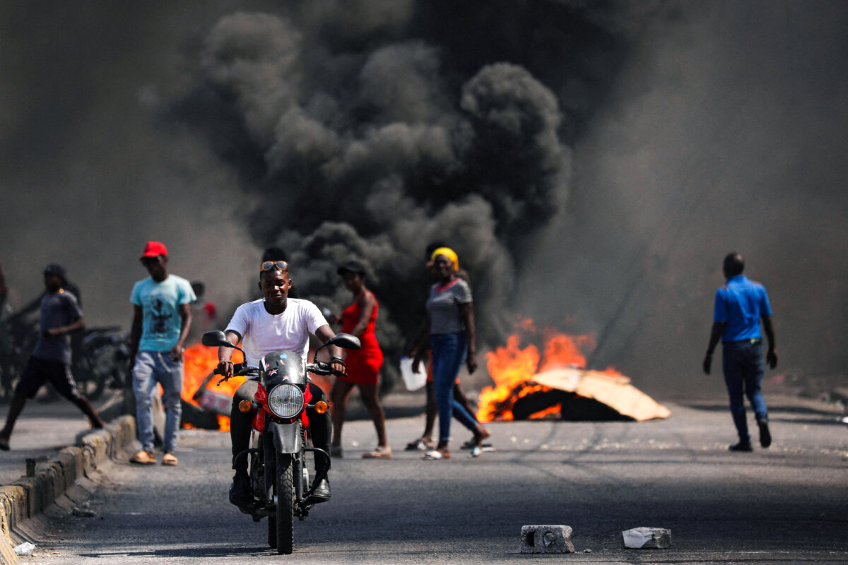 Một người đàn ông lái xe vượt qua một chướng ngại vật đang bốc cháy trong cuộc biểu tình phản đối chính phủ của Thủ tướng Ariel Henry và tình trạng bất ổn, ở Port-au-Prince, Haiti, hôm 01/03/2024. (Ảnh: Ralph Tedy Erol/Reuters)