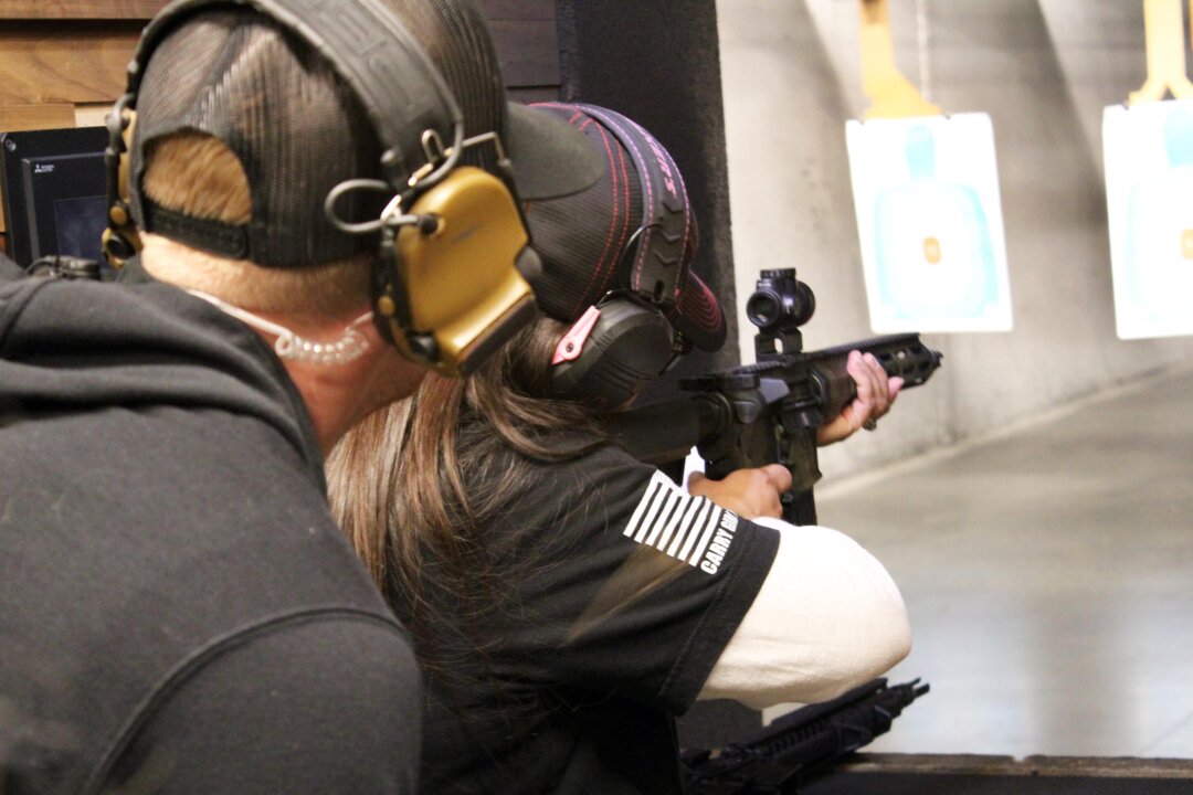 Một người tham dự Ngày Bắn súng Quốc gia dành cho Nữ giới đang bắn một khẩu súng trường bán tự động tại trường bắn trong nhà Texas Gun Experience, hôm 09/03/2024 trong lúc một nhân viên/người hướng dẫn tập bắn theo dõi. (Ảnh: Michael Clements/The Epoch Times)