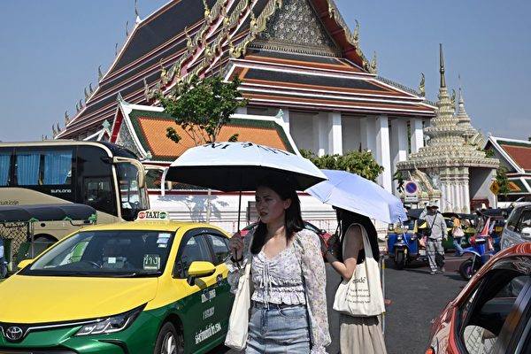 Du khách đứng ngoài chùa Wat Pho ở Bangkok dùng ô dù che chắn ánh nắng gay gắt, hôm 01/04/2024. (Ảnh: Lillian Suwanrumpha/AFP)