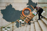 Một nhân viên đẩy xe trước một bảng hiệu cho thấy hoạt động của tập đoàn Evergrande Trung Quốc tại một khu chung cư của nhà phát triển địa ốc này ở Bắc Kinh ngày 08/12/2021. (Ảnh: Noel Celis/AFP qua Getty Images)