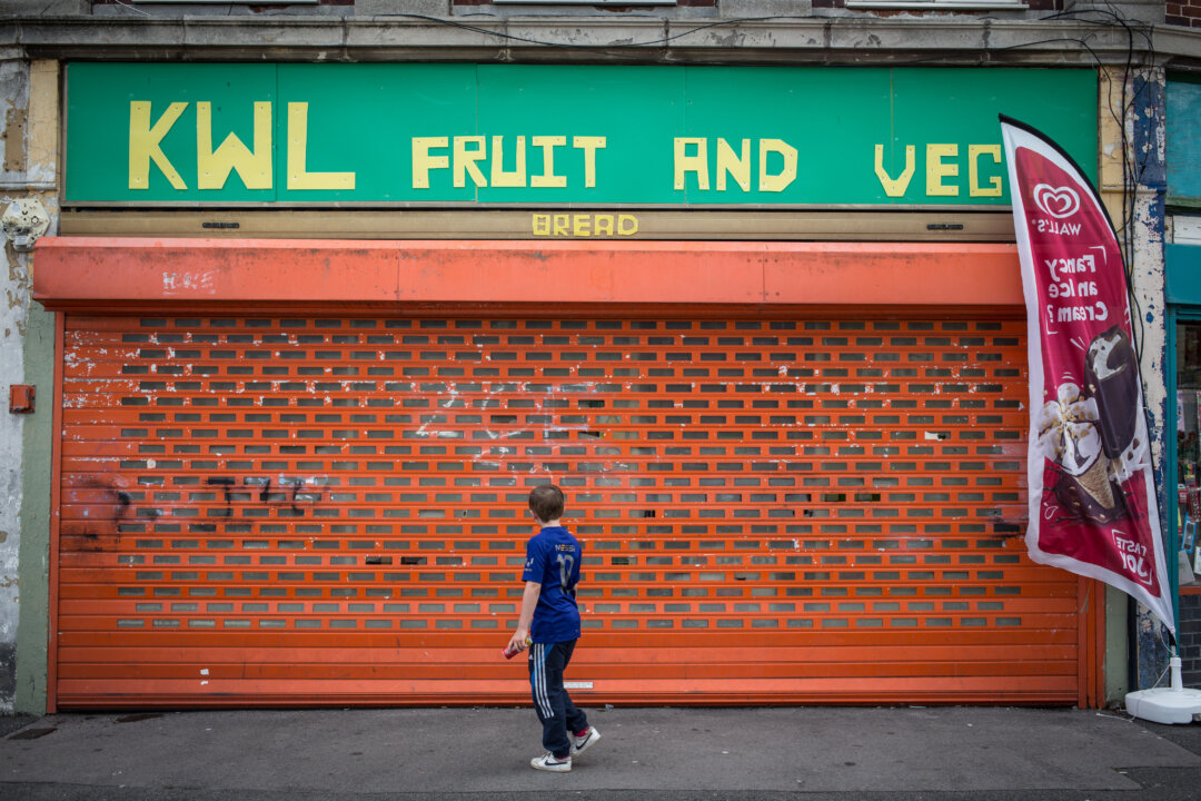 Một cậu bé đi ngang qua một cửa hàng đã đóng cửa trong khu nhà ở ở Bristol, Anh Quốc, vào ngày 03/08/2015. (Ảnh: Matt Cardy/Getty Images)